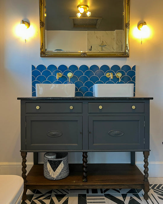 Free standing painted bathroom vanity with his and her sinks, gold hardware and a marble worktop. Blue mermaid tiles provide a beautiful splashback
